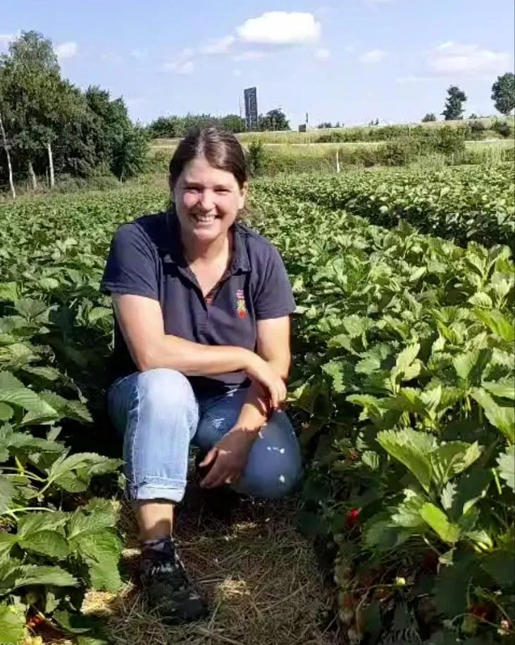 Mitarbeiterin von Erdbeerland kniet lachend zwischen den Erdbeerpflanzen in Wallerfangen