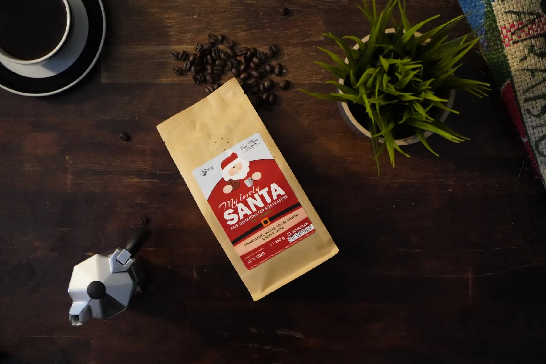 Kaffeetüte „Santa“ der Plaisir Kaffeemanufaktur neben Espressokanne und Kaffeebohnen